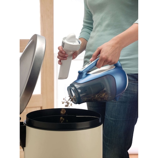 BLACKDECKER DV7210N handheld vacuum being emptied into a trash bin, close-up side view.