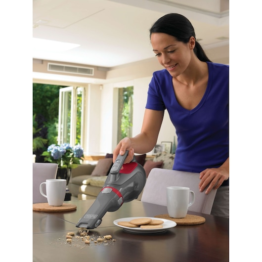 BLACKDECKER DV9610N handheld vacuum cleaning crumbs from a table near cups and cookies.