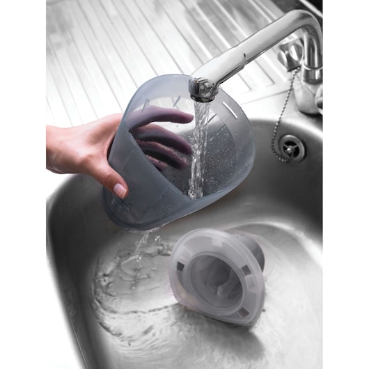 BLACKDECKER DV9610N vacuum filter container being rinsed under a chrome faucet in a kitchen sink.