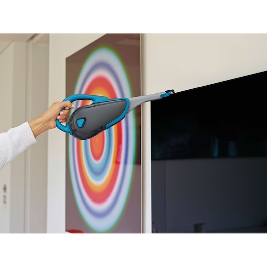 BLACKDECKER DVJ320J handheld vacuum with blue and gray design cleaning a TV screen.