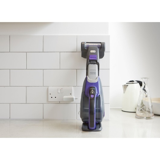 Photo of BLACKDECKER DVJ325BFSP handheld vacuum cleaner in purple on kitchen counter against white tile wall.