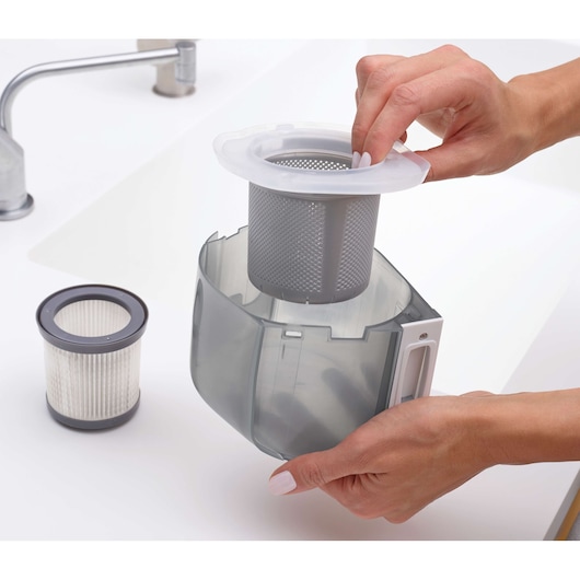 BLACKDECKER DVJ325BFS vacuum dust container with removable filter being cleaned near a sink.