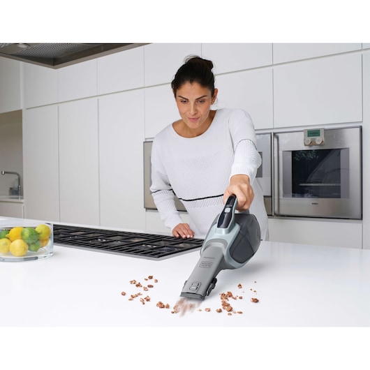 BLACKDECKER DVJ325J handheld vacuum cleaning crumbs from a white kitchen counter.