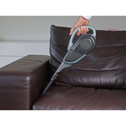 BLACKDECKER DVJ325J handheld vacuum cleaner cleaning a brown leather sofa, angled side view.