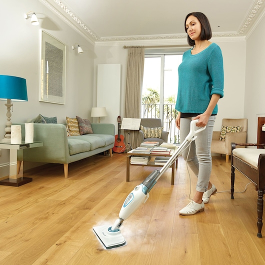 BLACK+DECKER FSM1605 steam mop cleaning wood floor in modern living room, photographed from the side.