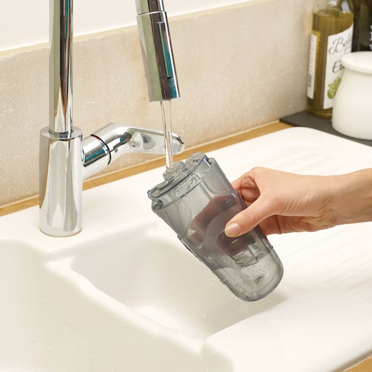BLACKDECKER FSM1605 water tank being rinsed under a faucet in a kitchen sink, close-up.