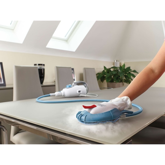 BLACK+DECKER FSMH13101SM steam cleaner used to clean a tabletop, white handheld unit and blue cleaning glove visible.