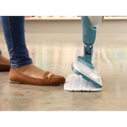 Photo of BLACKDECKER FSMH13101SM steam mop with cleaning pad being attached by foot, shown on a polished floor.