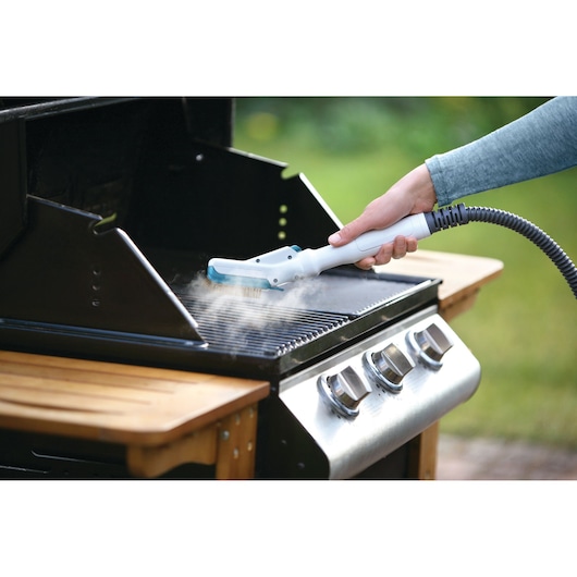 BLACKDECKER FSMH13101SM steam cleaner attachment cleaning a barbecue grill rack outdoors.