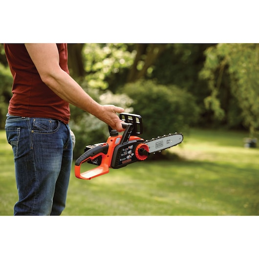 Photo of BLACK+DECKER GKC1825L20 cordless chainsaw with 25cm bar held outdoors in a garden.