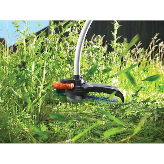BLACKDECKER GL7033 grass trimmer cutting tall vegetation in outdoor garden, close-up view.