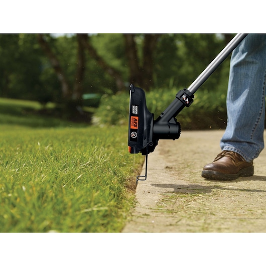 BLACKDECKER GLC3630L20 grass trimmer in use edging lawn, close-up view of cutting head and guard.