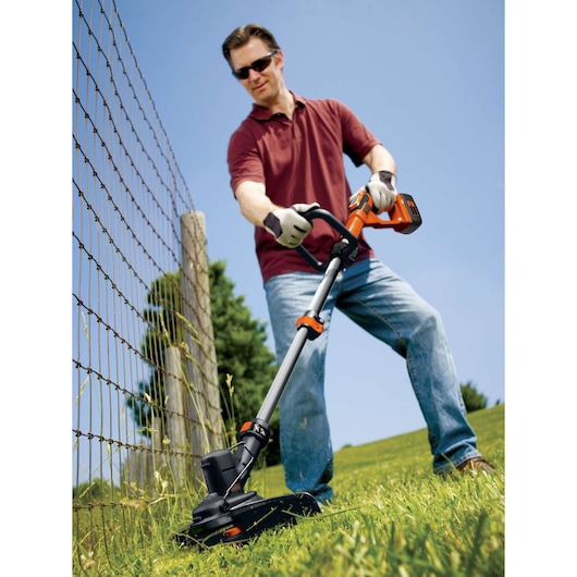 BLACKDECKER GLC3630L20 cordless grass trimmer in use near a fence outdoors on a sunny day.
