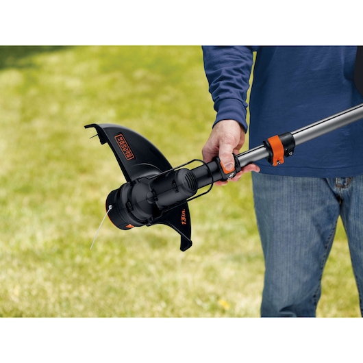 Photo of BLACK+DECKER GLC3630L20 grass trimmer being held by a person outdoors on grass, close-up on cutting head.