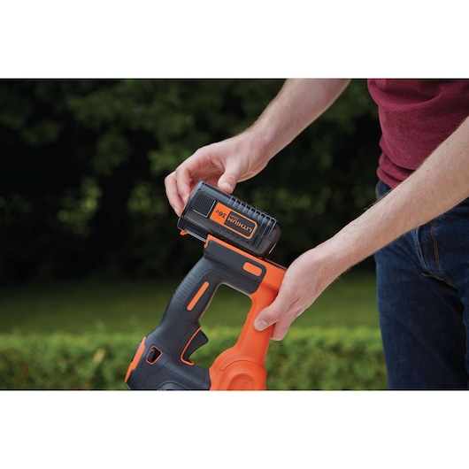 Photo of BLACKDECKER GTC36552PC hedge trimmer with 36V lithium battery being inserted outdoors.