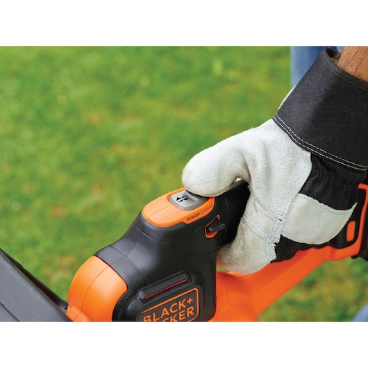 Photo of gloved hand using BLACK+DECKER GTC36552PC hedge trimmer, showing close-up of PowerCommand button.