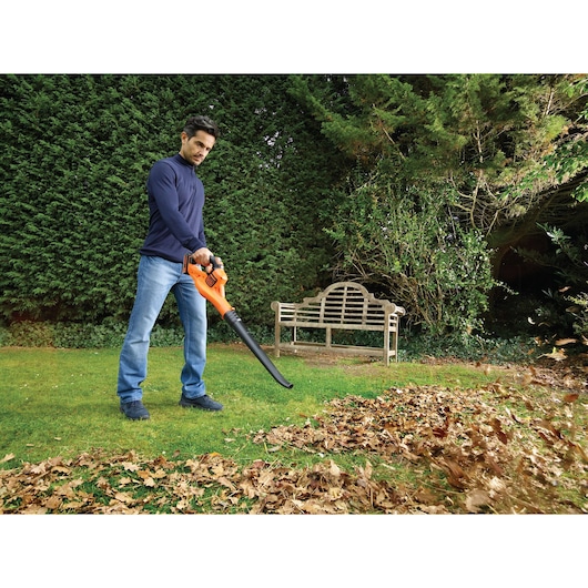 BLACKDECKER GWC1820PC cordless leaf blower used in a garden to clear fallen leaves.