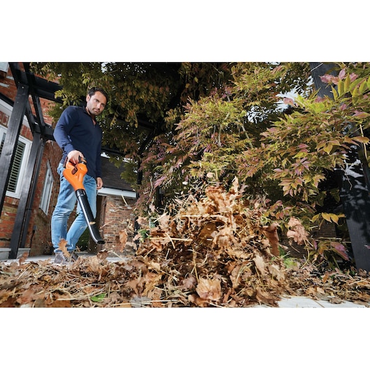 BLACKDECKER GWC1820PC leaf blower clearing dry leaves on patio, held by person in garden.