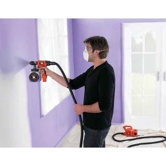 BLACKDECKER HVLP400 paint sprayer used indoors for wall painting, visible hose and unit on floor.