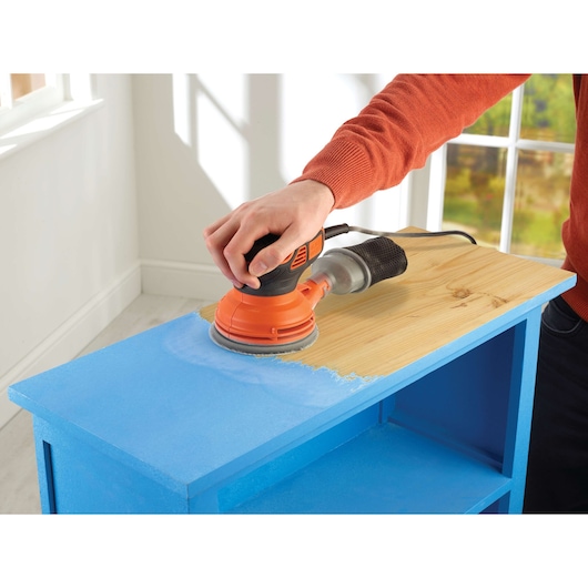 Photo of BLACKDECKER KA199 sander used to remove blue paint from a wooden shelf in a bright room.