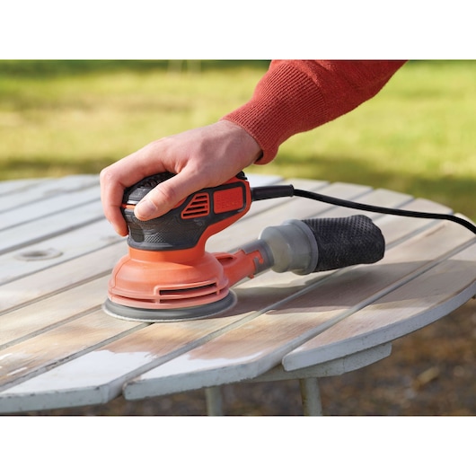 Photo of BLACKDECKER KA199 random orbital sander being used on a wooden outdoor table.