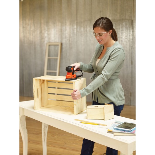BLACKDECKER KA2000 sander used on a wooden crate in workshop setting, with tools and books on white table.