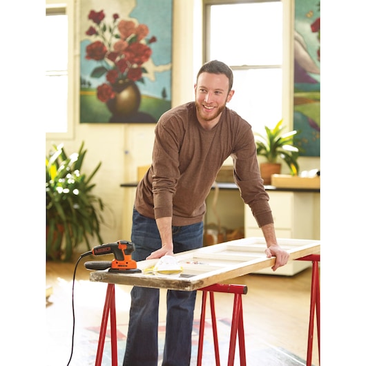 BLACKDECKER KA2000 detail sander on workbench next to person working on wooden frame in bright indoor space.