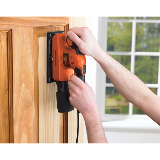 Photo of BLACKDECKER KA274EKA electric sander in use on a wooden door, shown in a home setting.