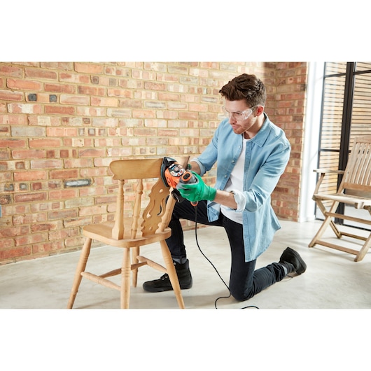 Photo of a person sanding a wooden chair with a BLACK+DECKER KA280LSA multi-sander in a workshop setting.
