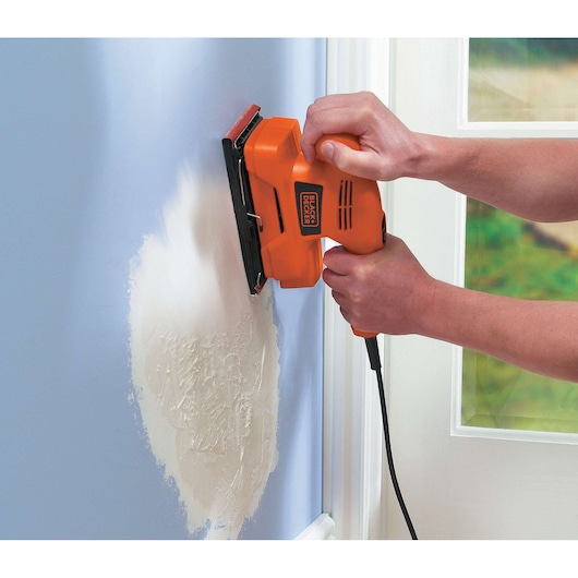 BLACKDECKER KA300 detail sander in use on a wall, orange and black handheld tool.