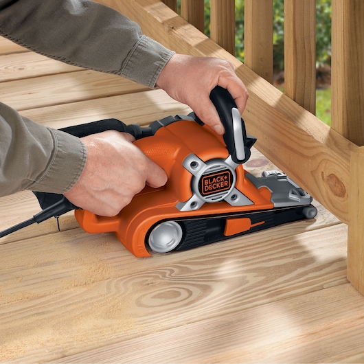 BLACKDECKER KA88 belt sander in use sanding wooden decking, orange and black design, product photography.