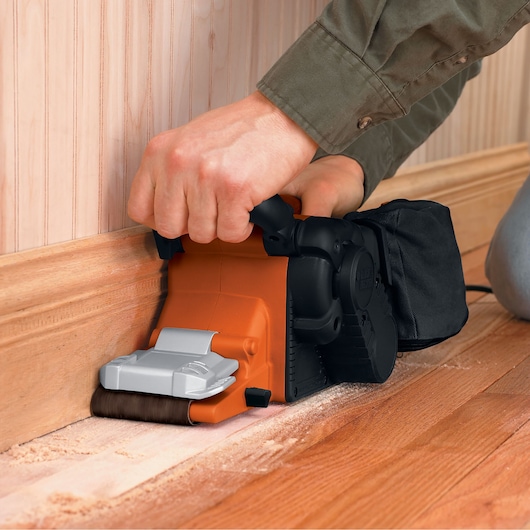 BLACKDECKER KA88 belt sander sanding wooden floor near baseboard, close-up side angle.
