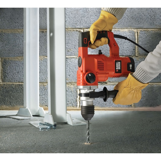 BLACKDECKER KD1250K rotary hammer drill being used to drill into concrete, close-up with gloves.