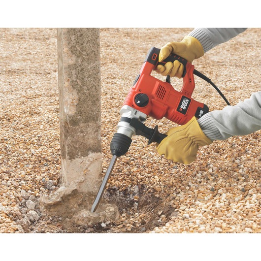 Photo of BLACK+DECKER KD1250K rotary hammer drill in use on a concrete post outdoors, gloved hands holding the tool.