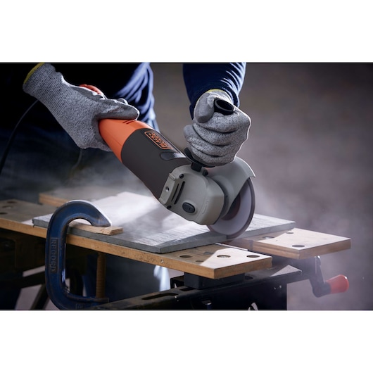BLACKDECKER KG1202K angle grinder in use on a workbench, worker wearing gloves, producing dust while cutting.