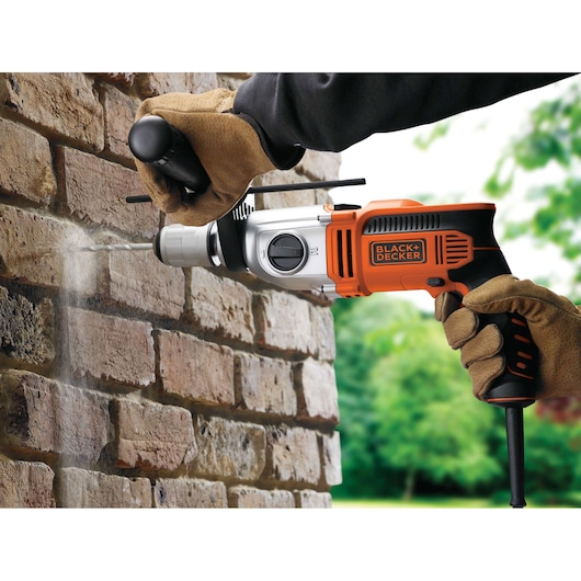 BLACK+DECKER KR911K hammer drill in use on a brick wall, orange and black design, user wearing gloves.