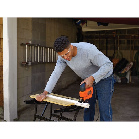 BLACKDECKER KS701E jigsaw used to cut PVC pipe on workbench in a garage setting.