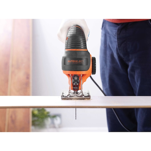 BLACKDECKER KS901SEK jigsaw cutting wood, close-up front view, orange and black body, user wearing glove.