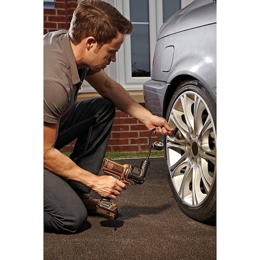 BLACKDECKER MTNF9 portable inflator in use on a car tire outdoors.