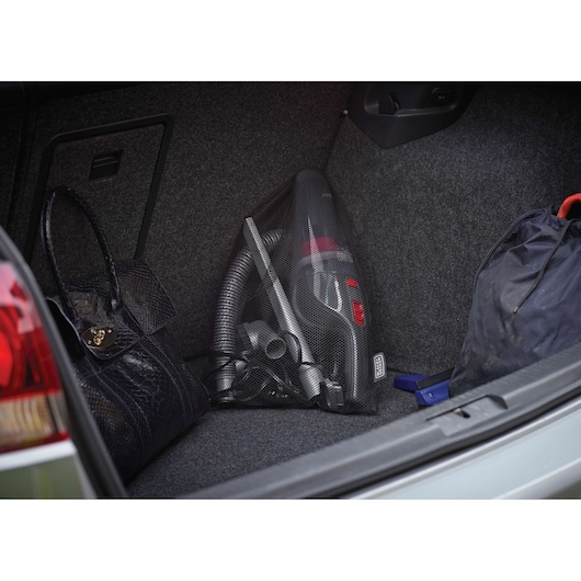 BLACK+DECKER NV1210AV handheld vacuum in a car trunk beside bags, showing compact storage.