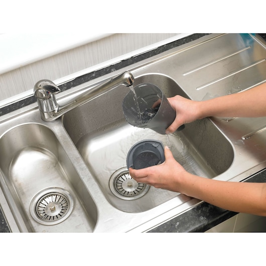 BLACKDECKER NV2410N vacuum filter and dust container being rinsed under faucet in stainless steel sink.