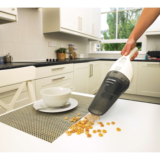 BLACK+DECKER NV2420N handheld vacuum cleaner picking up cereal from a kitchen table, bowl and spoon nearby.