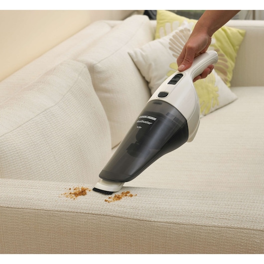 BLACK+DECKER NV4820N handheld vacuum cleaner removing crumbs from a beige sofa, angled side view.