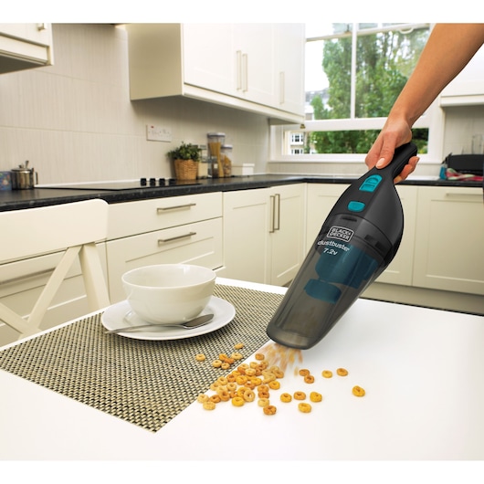BLACK+DECKER NV7210N handheld vacuum cleaner cleaning cereal from kitchen table, side angle.