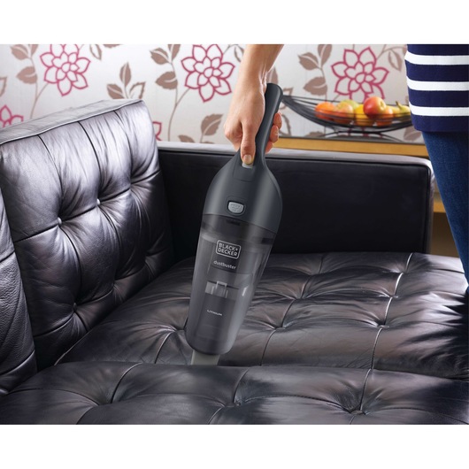 Photo of BLACKDECKER NVB215WA handheld vacuum cleaning a black leather sofa.