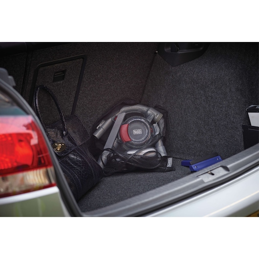 BLACK+DECKER PD1200AV portable car vacuum in car trunk, gray and red, with bag and accessories visible.