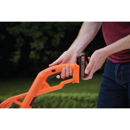 BLACKDECKER ST182320 grass trimmer handle with person inserting 18V lithium battery outdoors.