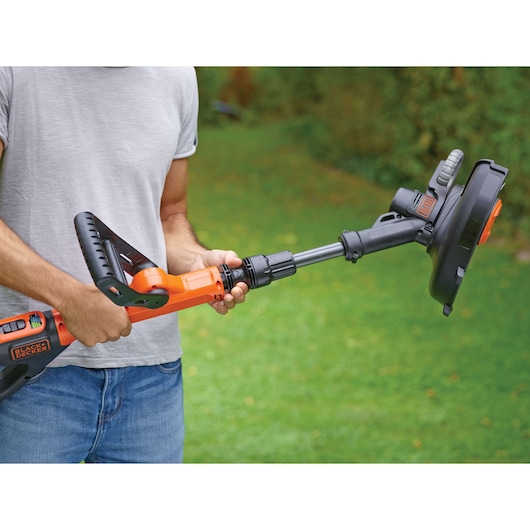 Photo of person holding BLACKDECKER STC1820PC cordless grass trimmer, orange and black, in a garden.