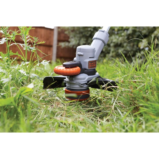 Photo of BLACK+DECKER STC1820 grass trimmer in use, close-up of cutting head trimming garden grass.