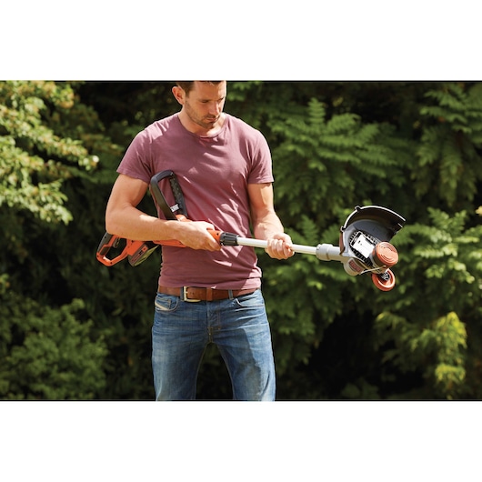 Man holding BLACKDECKER STC1820 cordless grass trimmer in garden, close-up view on trimmer and handle.